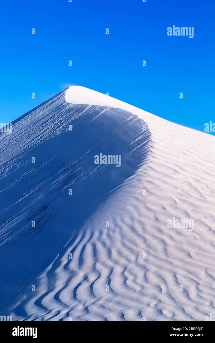 Wind weht Sand an der Spitze einer Sanddüne. Abstraktes Bild, das helle und dunkle Seiten zeigt Stockfoto
