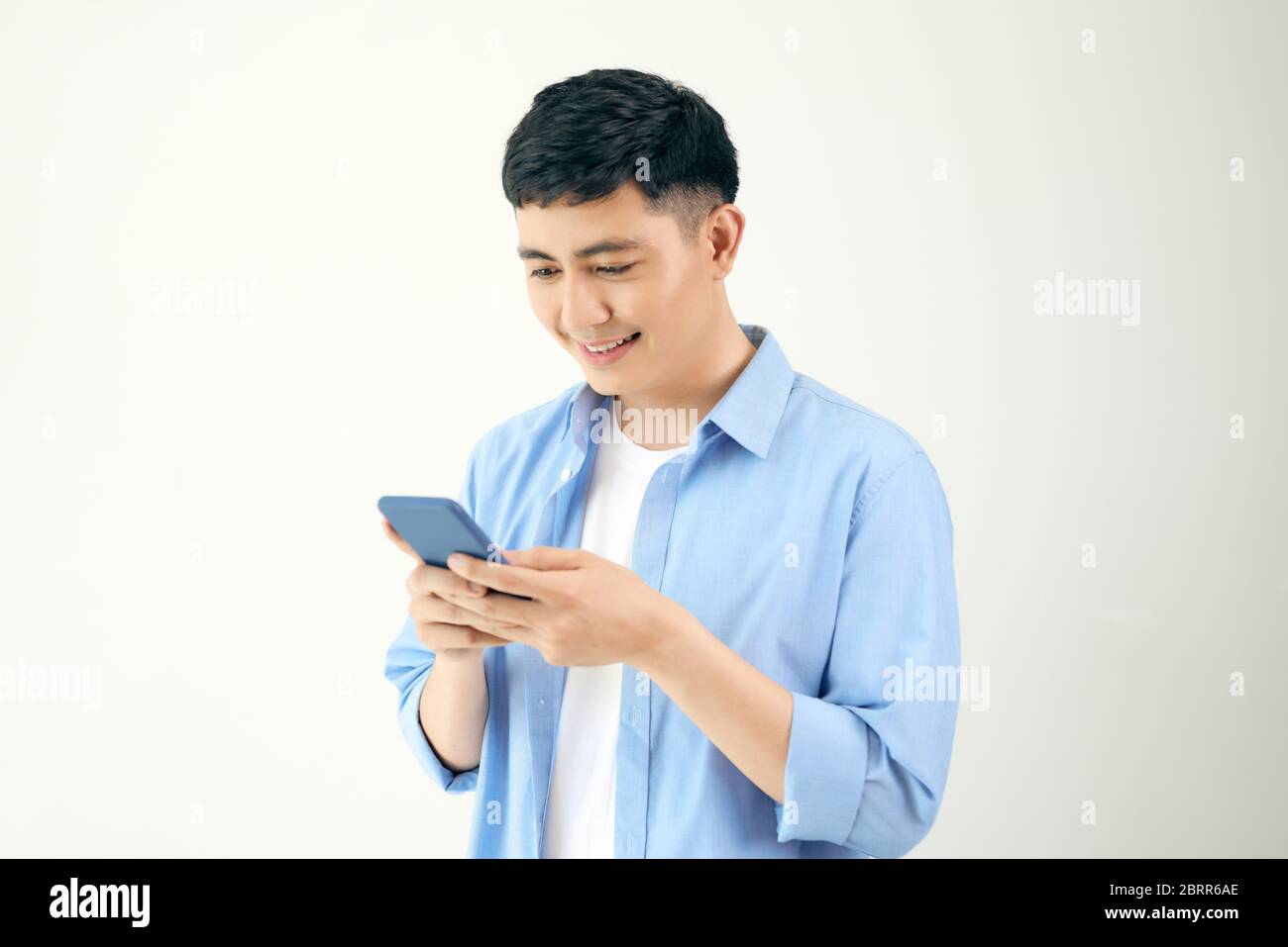 Entspannter junger Mann, der auf dem Handy eine Textnachricht liest, isoliert auf weißem Studiohintergrund. Stockfoto