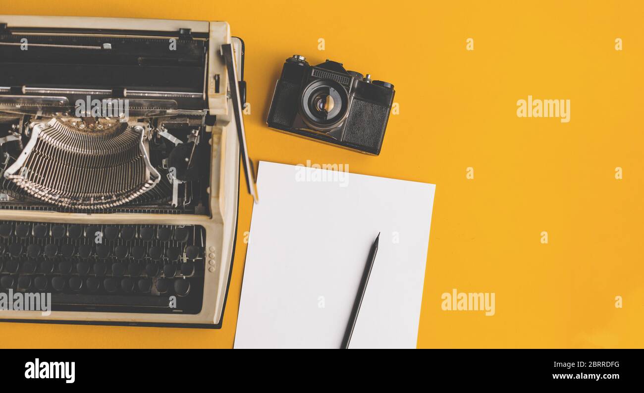 Schreibmaschine, Retro-Filmkamera, Blatt Papier und Bleistift auf gelbem Hintergrund, Draufsicht mit Kopierraum. Kreatives Konzept Stockfoto