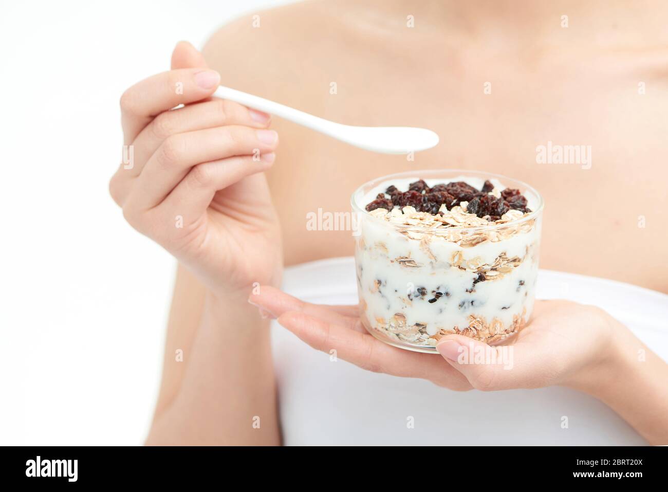 Gesunde Essende Frau. Nahaufnahme der schönen fröhlichen jungen Frau, die morgens ein Glas mit Naturjoghurt, köstlicher Rosine und Müsli hält Stockfoto