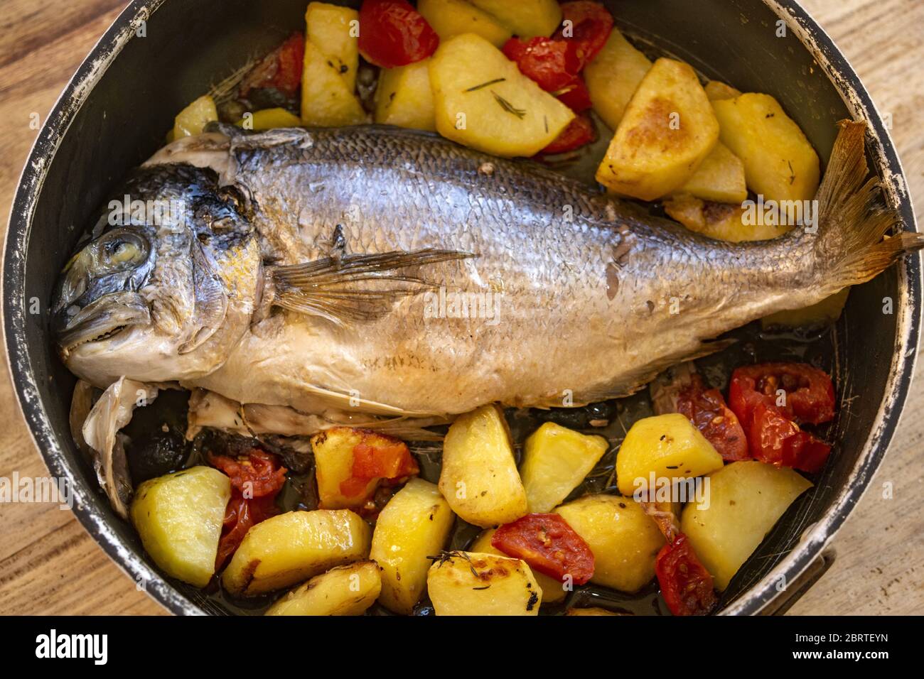Gebackene Brassen mit Kartoffeln und Tomaten in einer Backform Stockfoto