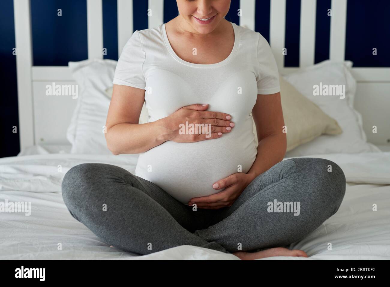 Schwangere Frau sitzt auf dem Bett und hält die Hände auf dem Bauch Stockfoto