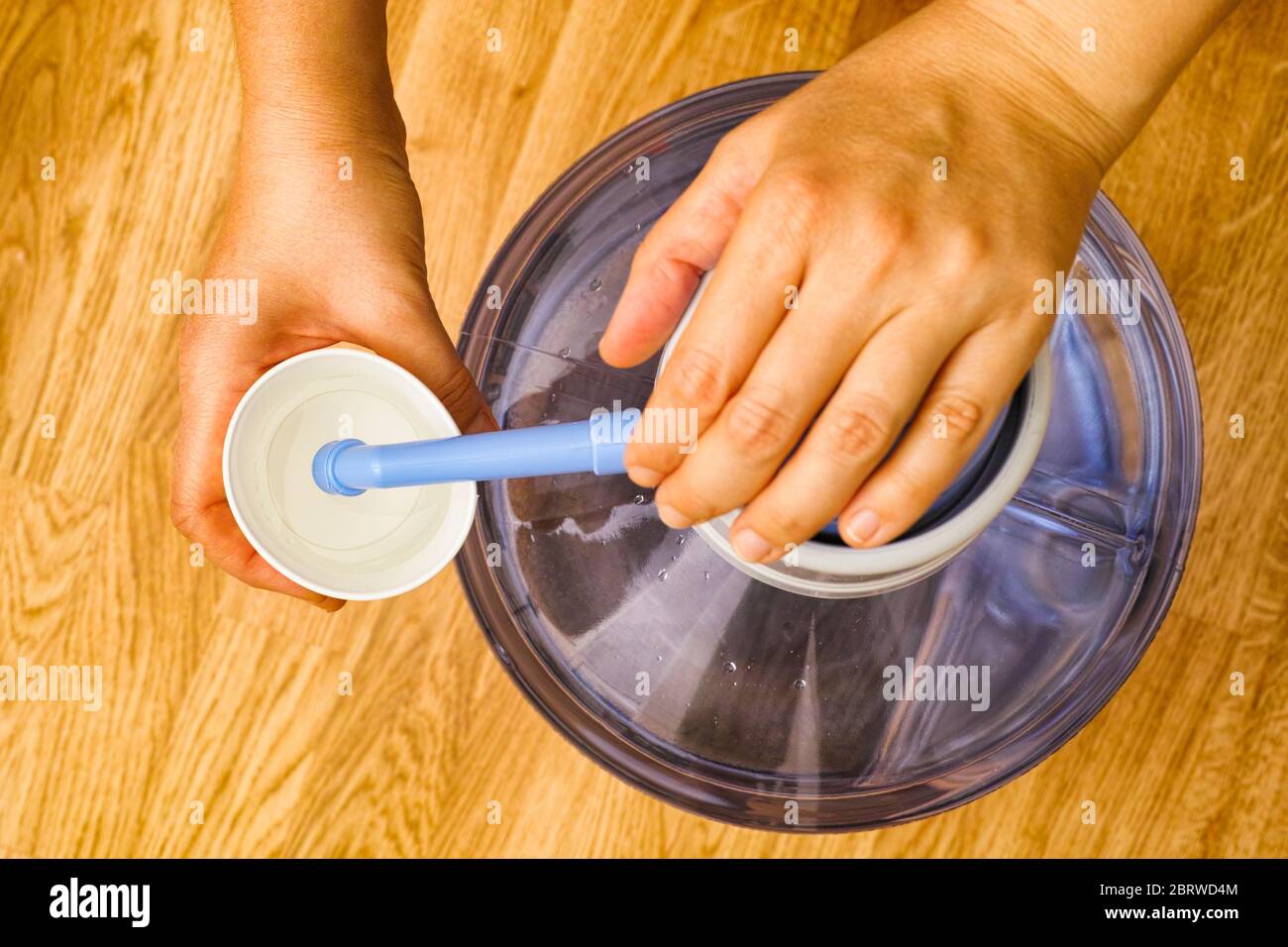 Person Hände gießen Wasser in Papierbecher aus der Flasche mit Wasserpumpe. Draufsicht. Stockfoto