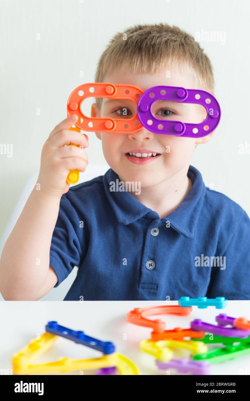 Liebenswert junge gemacht Gläser aus Kunststoff Block Spielzeug und lächelnd. Vertikale Foto von lustigen kreativen Kleinkind Stockfoto