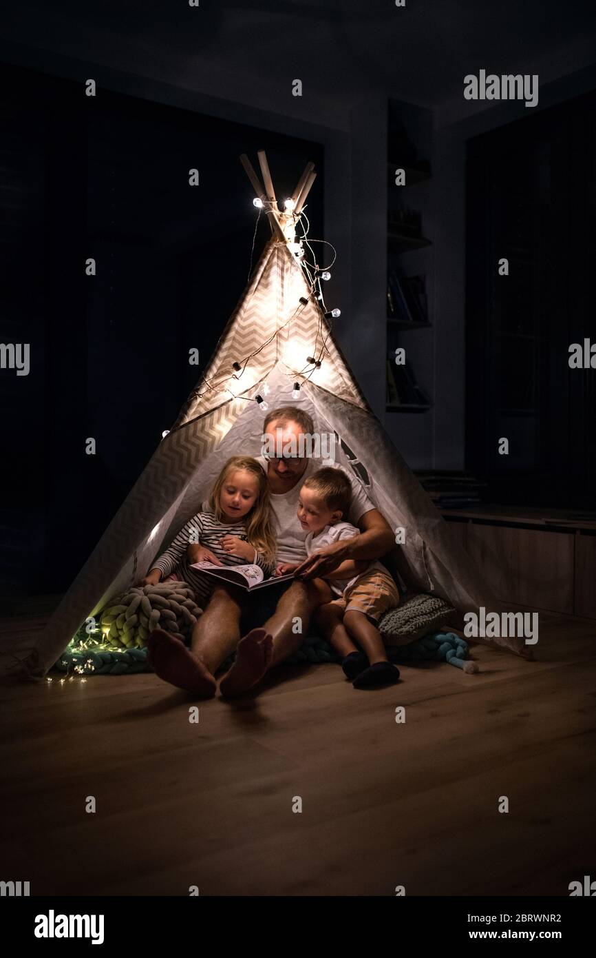 Vater mit Kindern, die drinnen im Schlafzimmer sitzen und ein Buch lesen. Stockfoto