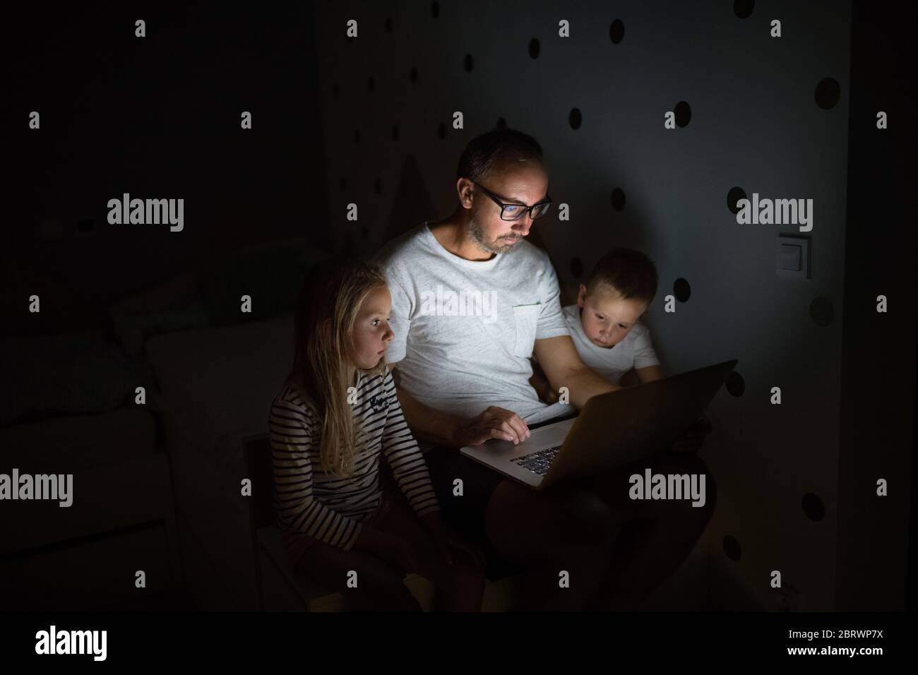 Vater mit Kindern, die drinnen im Schlafzimmer sitzen, mit Laptop. Stockfoto