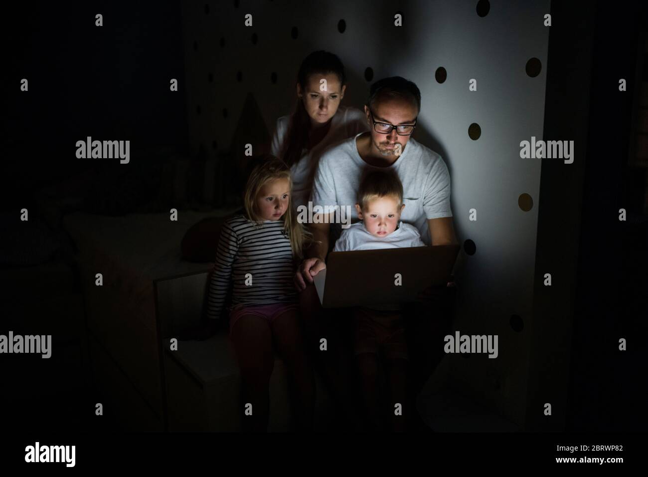 Familie mit Kindern, die im Schlafzimmer sitzen und einen Laptop benutzen. Stockfoto