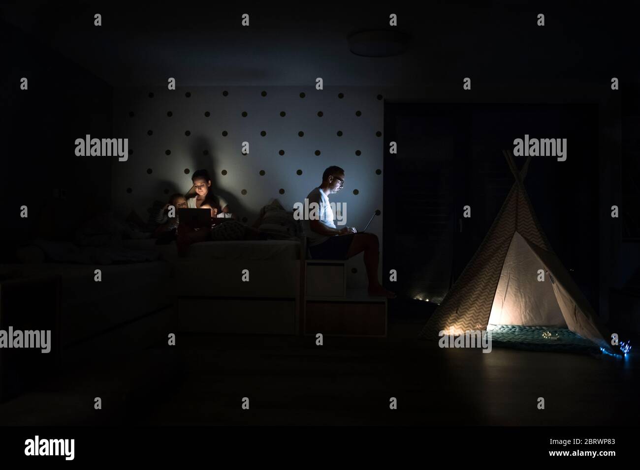 Familie mit Kindern, die im Schlafzimmer sitzen und einen Laptop benutzen. Stockfoto