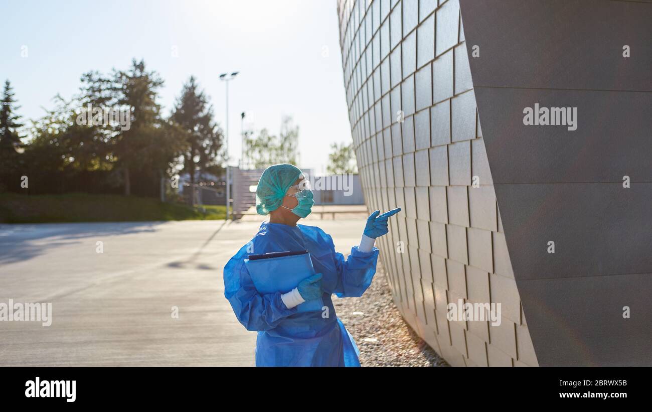 Der Containment Scout vor der Klinik macht Handsignale am Eingang zur Einlasskontrolle während der Coronavirus-Pandemie Stockfoto