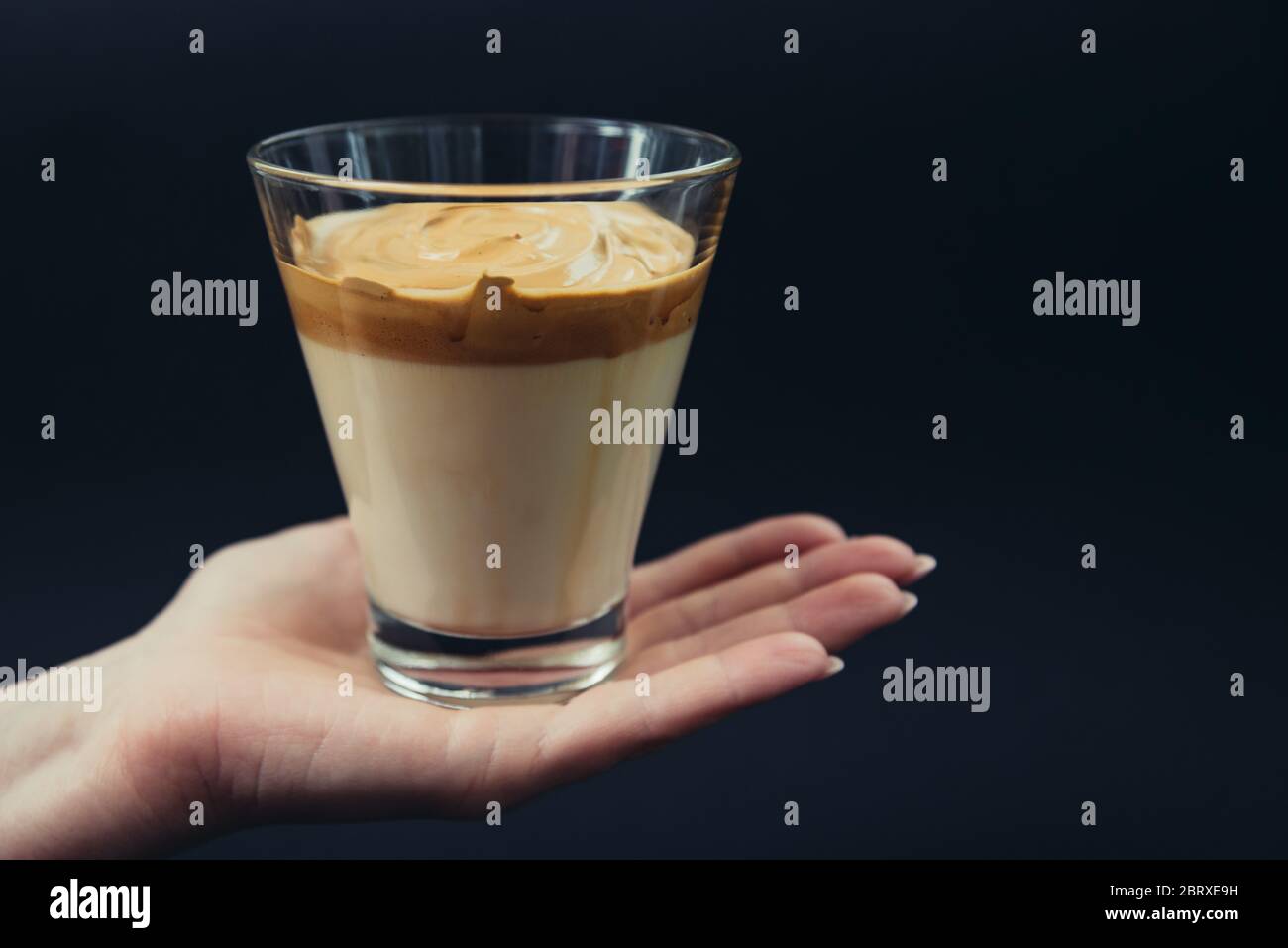 Frau Hand hält trendy koreanischen Dalgona Kaffee zu Hause gemacht. Schwarzer Boden Stockfoto