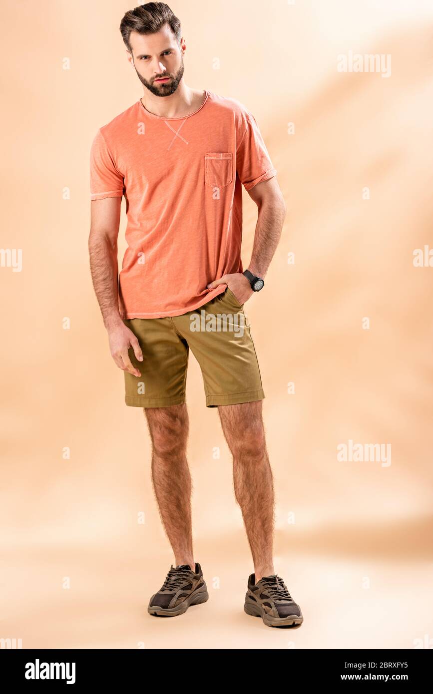 Modischer Mann posiert in Shorts und Sommer-T-Shirt auf beige Stockfoto
