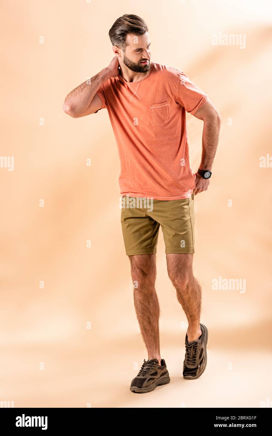 Stylischer, schöner Mann posiert in Shorts und Sommer-T-Shirt auf beige Stockfoto