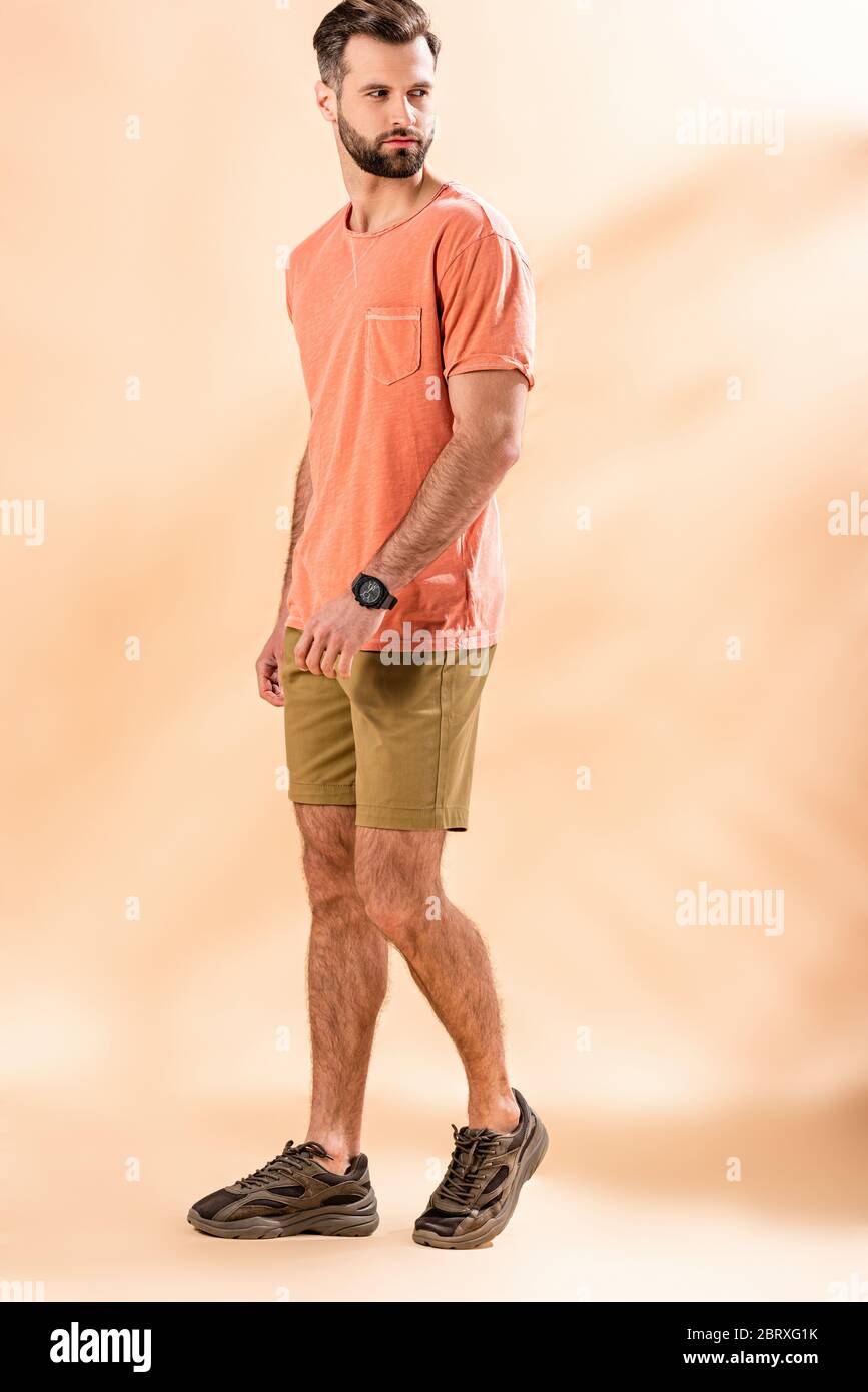 Schöner, stylischer Mann posiert in Shorts und Sommer-T-Shirt auf beige Stockfoto