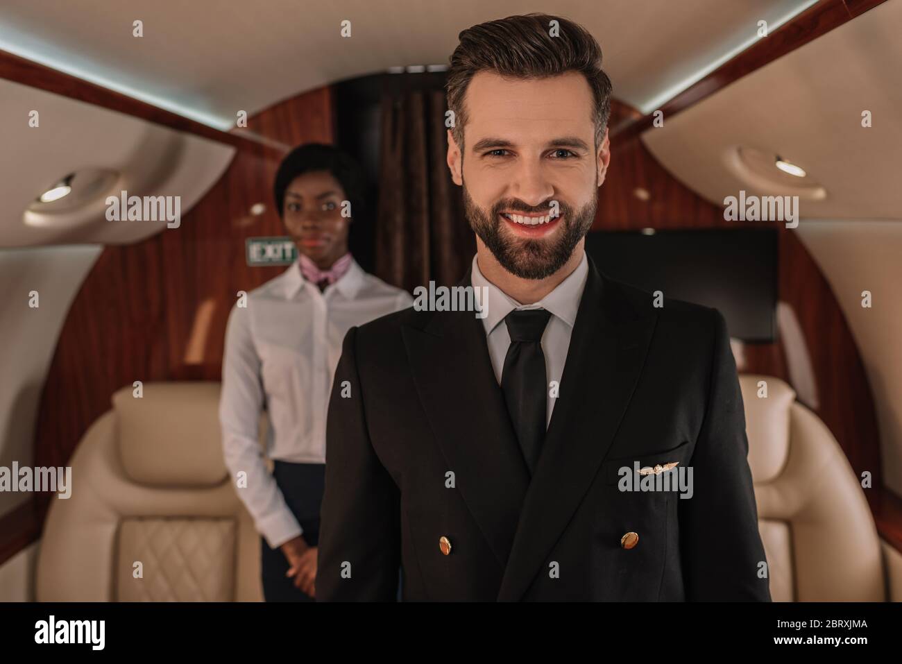 Selektiver Fokus des hübschen Piloten lächelt in der Nähe der afroamerikanischen Stewardess Stockfoto