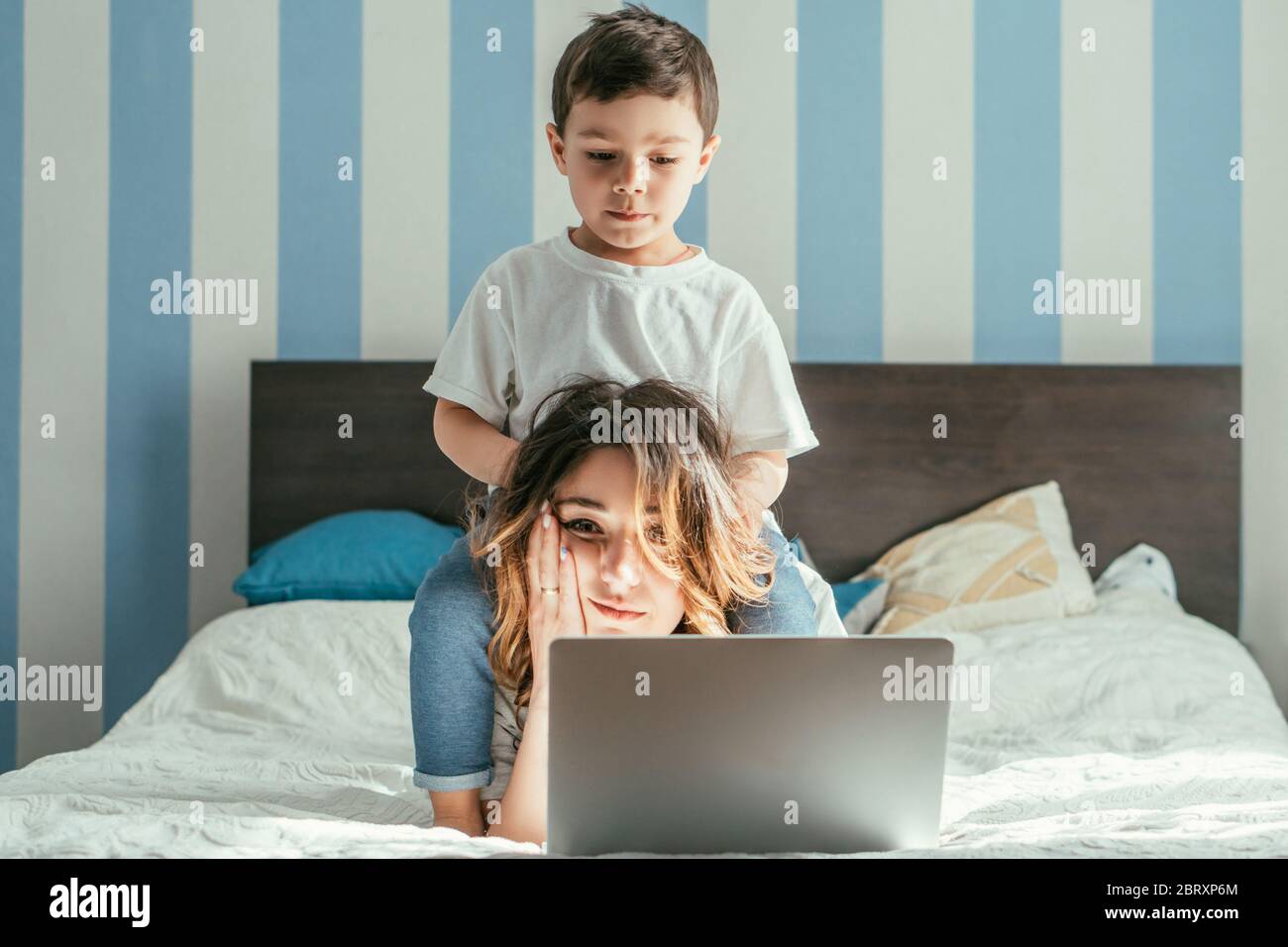 Kleinkind Junge berühren Haare von müde Freelancer Mutter im Schlafzimmer Stockfoto