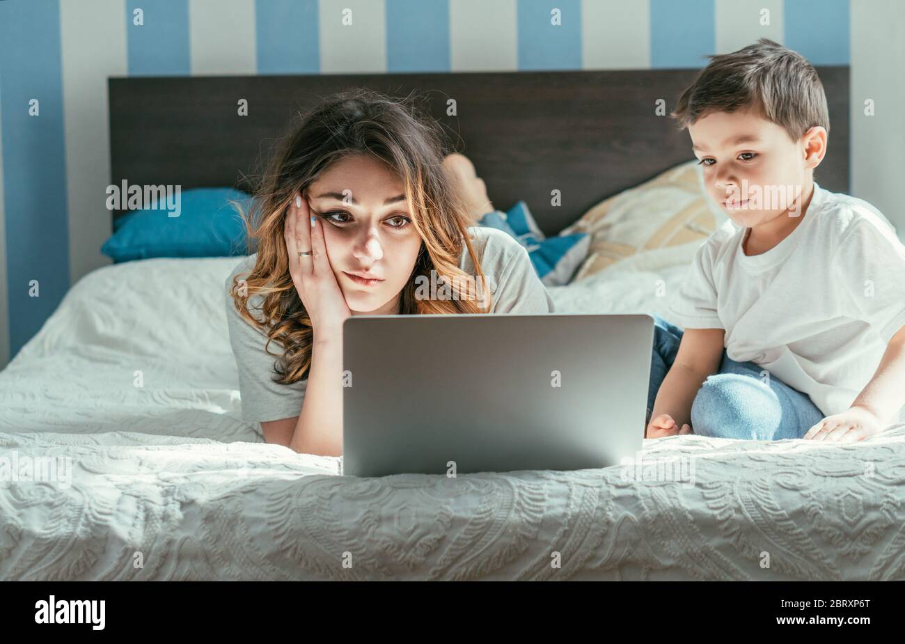 Kleinkind Junge sitzt auf dem Bett in der Nähe müde Freelancer Mutter von zu Hause aus Stockfoto