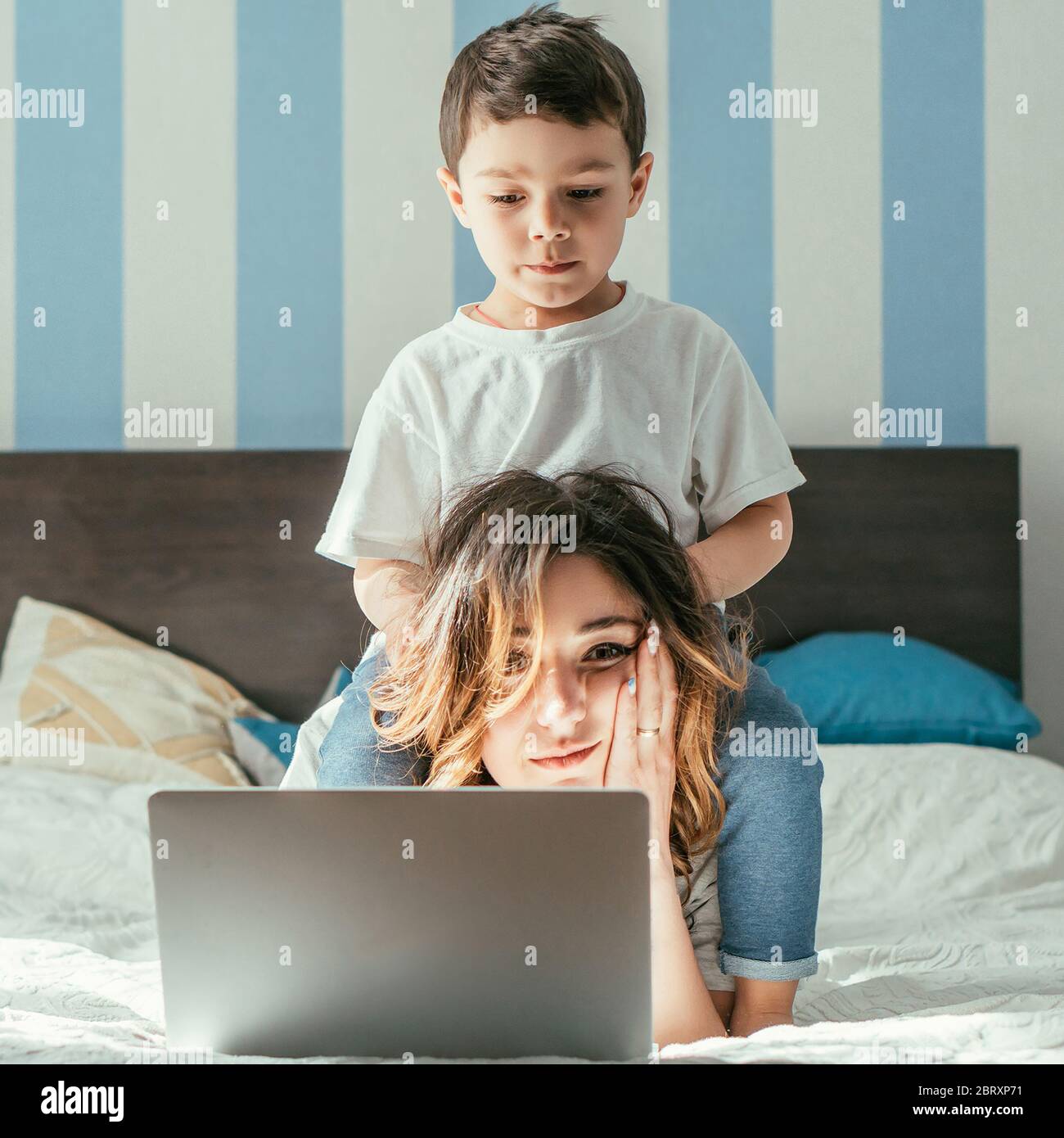 Niedlichen Kleinkind junge berühren Haar von müde Freelancer Mutter in der Nähe Laptop im Schlafzimmer Stockfoto