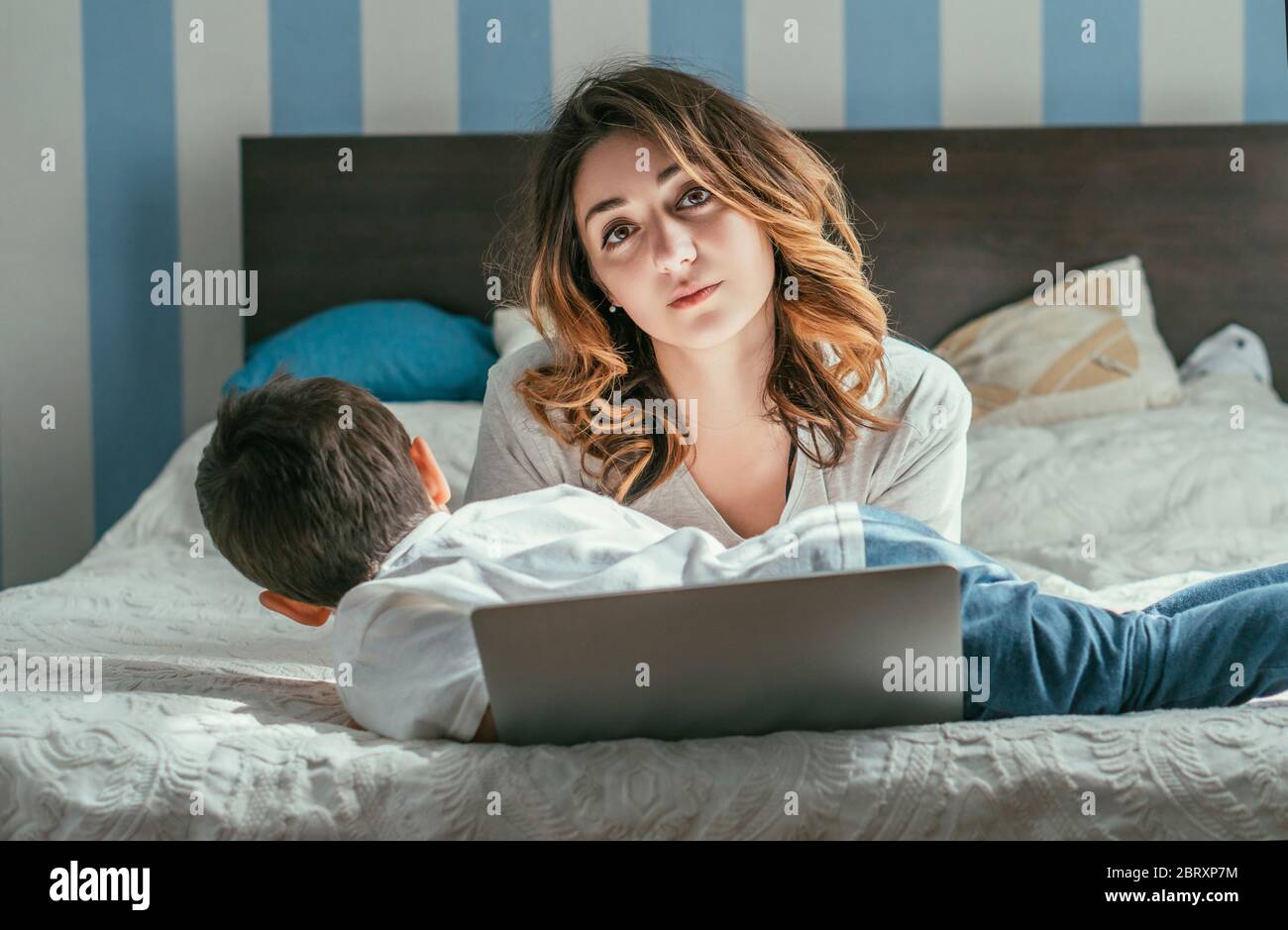 Kleinkind Junge liegt auf dem Bett in der Nähe müde Freelancer Mutter und Laptop Stockfoto