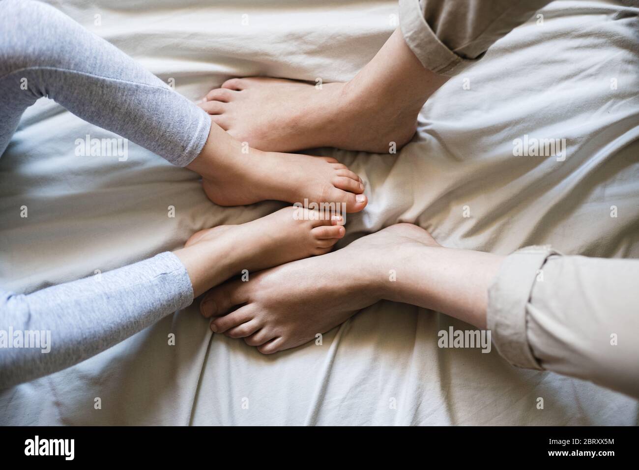 Mutter und Kind kreuzen ihre Füße zusammen, während sie auf beigefarbenen Bettlaken sitzen. Es ist ein zarter Moment, wenn sie vergleichen, wie ähnlich sie sind Stockfoto
