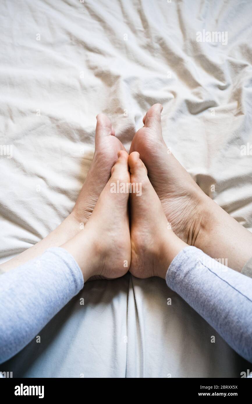 Mutter und Kind verbinden sich die Füße, während sie auf beigefarbenen Bettlaken sitzen. Es ist ein zarter Moment, wenn sie vergleichen, wie ähnlich sie sind. Nahaufnahme Stockfoto