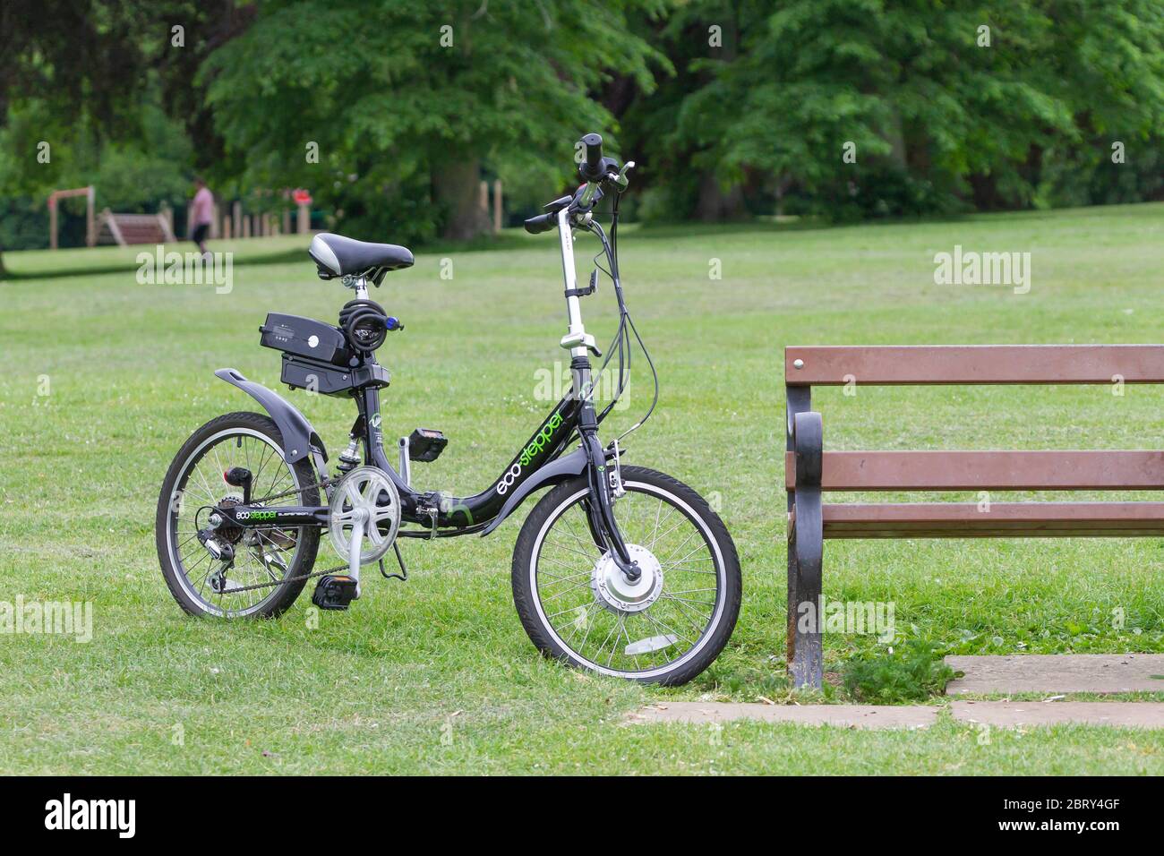 Eco-Stepper E-Bike auf Stand, während die Fahrerdame auf einer Parkbank in  Abington Park, Northampton, England, Großbritannien sitzt Stockfotografie -  Alamy