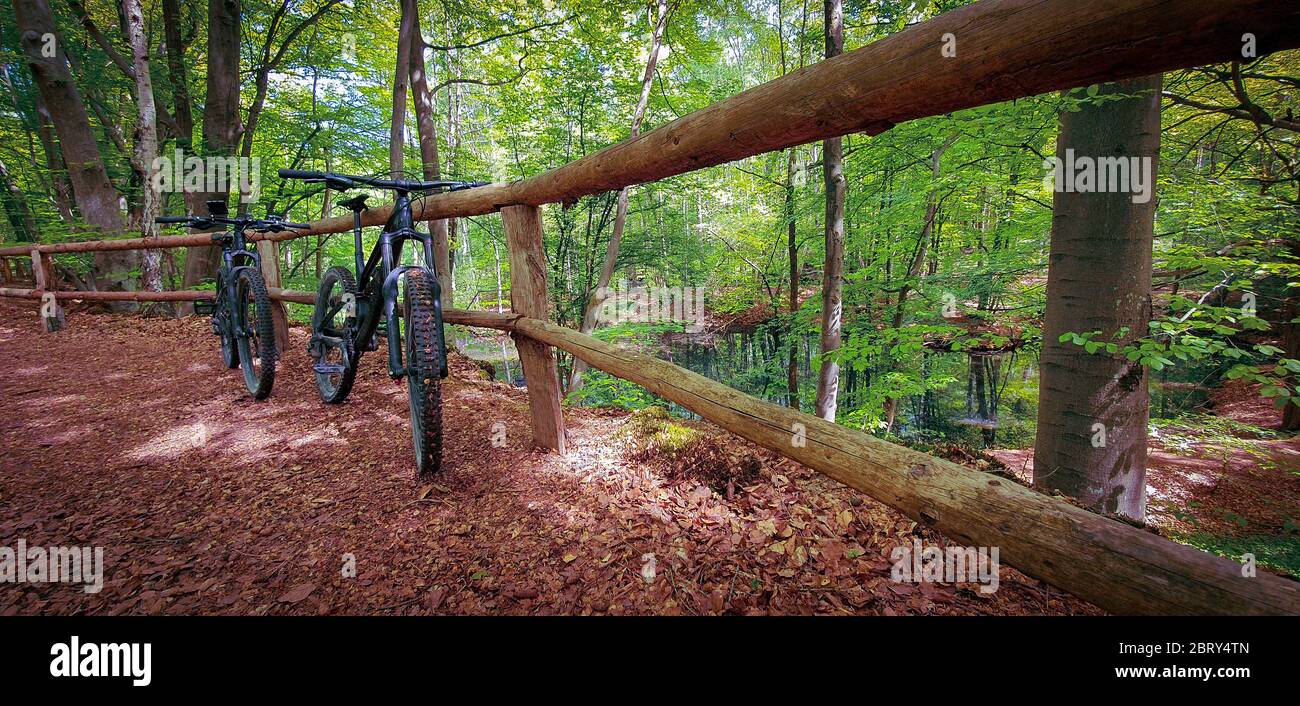 Zwei Mountainbikes auf einem Holzzaun neben einem schönen kleinen See auf einem grünen Waldweg. Mountainbike-Konzept. Freiheitskonzept. Stockfoto