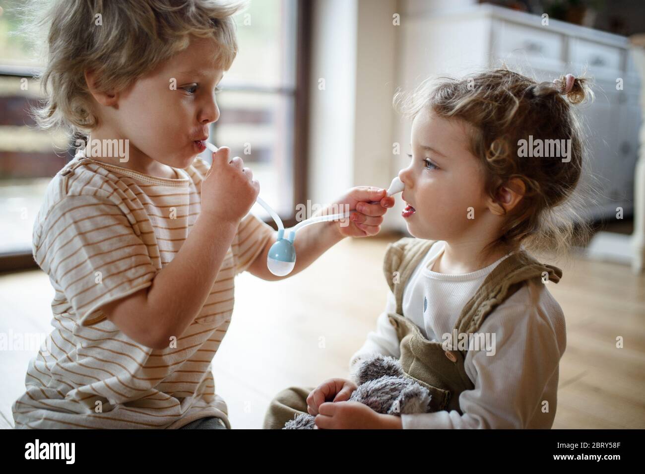 Zwei kleine Kinder, Bruder und Schwester zu Hause, spielen mit Nasal-Aspirator. Stockfoto