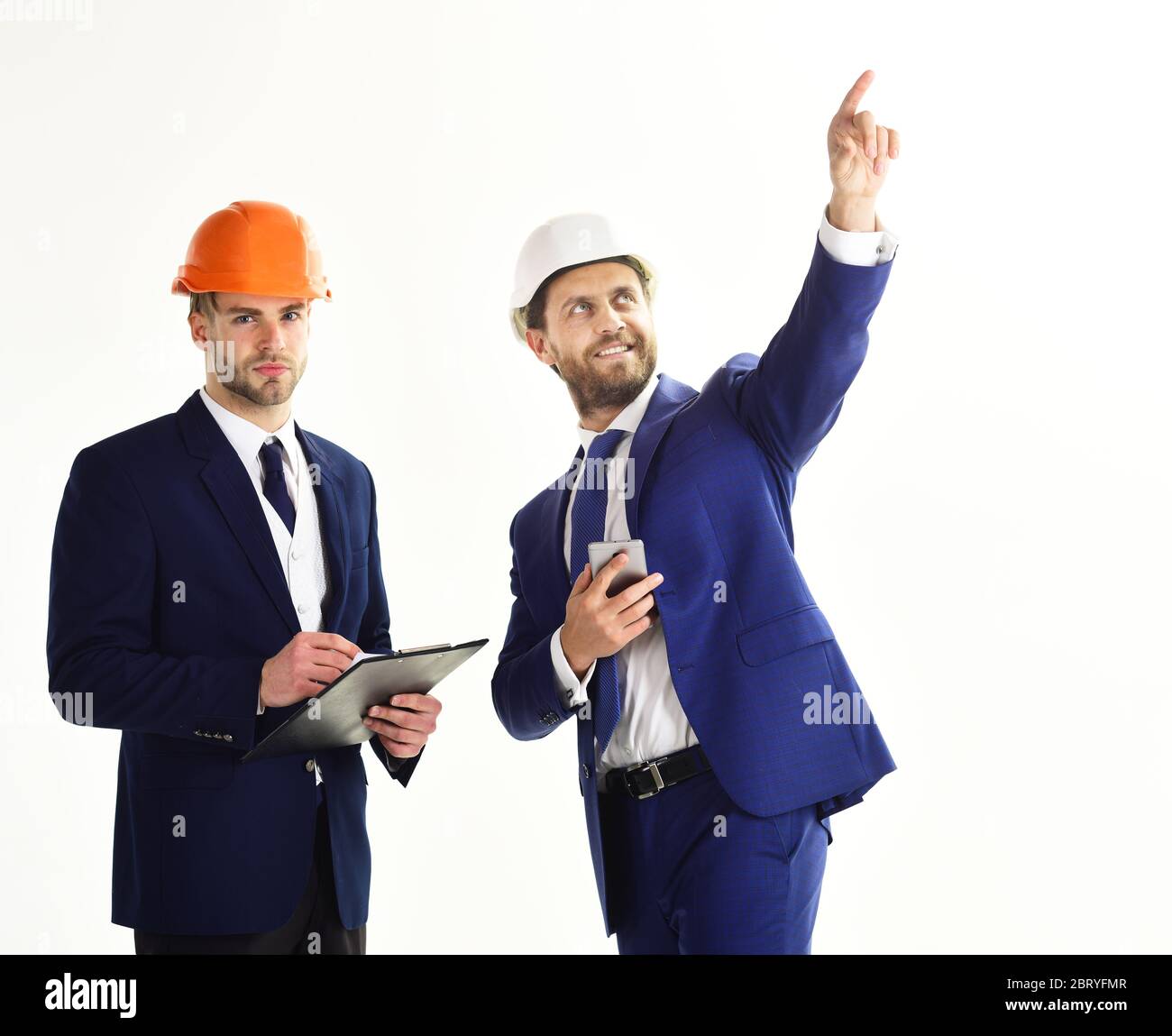 Mitarbeiter, Engineering, Erfolgskonzept. Mann zeigt etwas mit dem Finger. Bauingenieur und Baumeister mit ruhigen und lächelnden Gesichtern. Bauleiter und Bauleiter in Helmen. Stockfoto