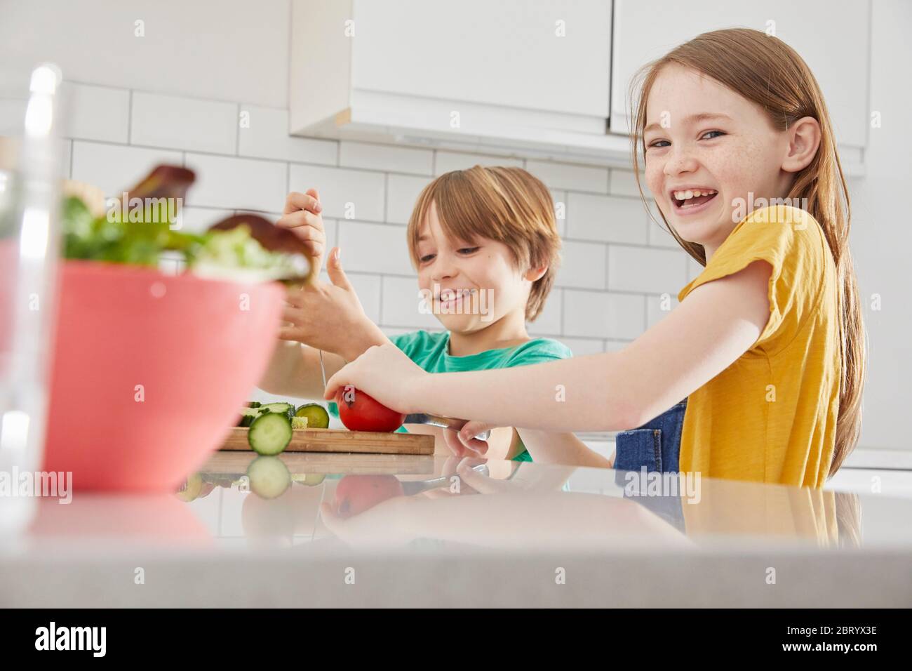 Junge und Mädchen stehen in einer Küche, schneiden englische Gurken und Tomaten. Stockfoto