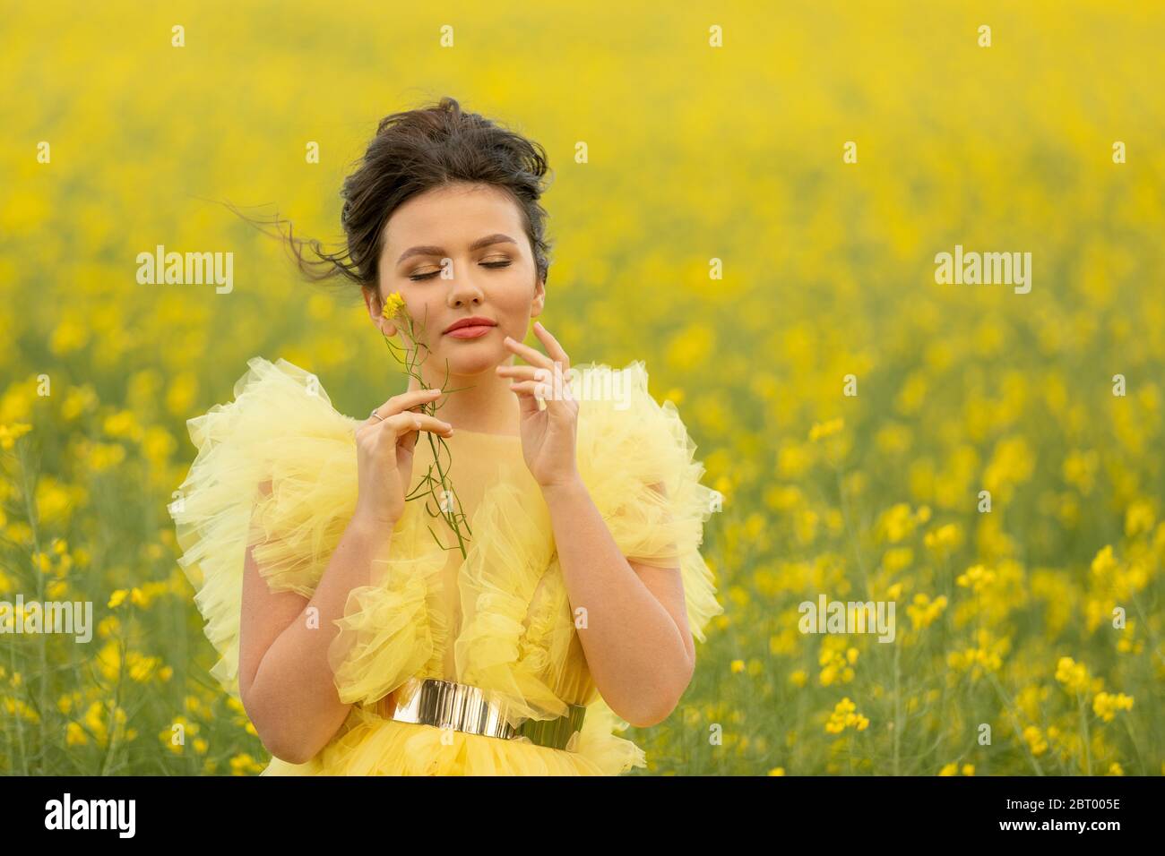 Porträt von romantischen Brünette jugendlich Mädchen trägt bei gelben Kleid posiert auf Feld mit gelben Raps Blumen Stockfoto
