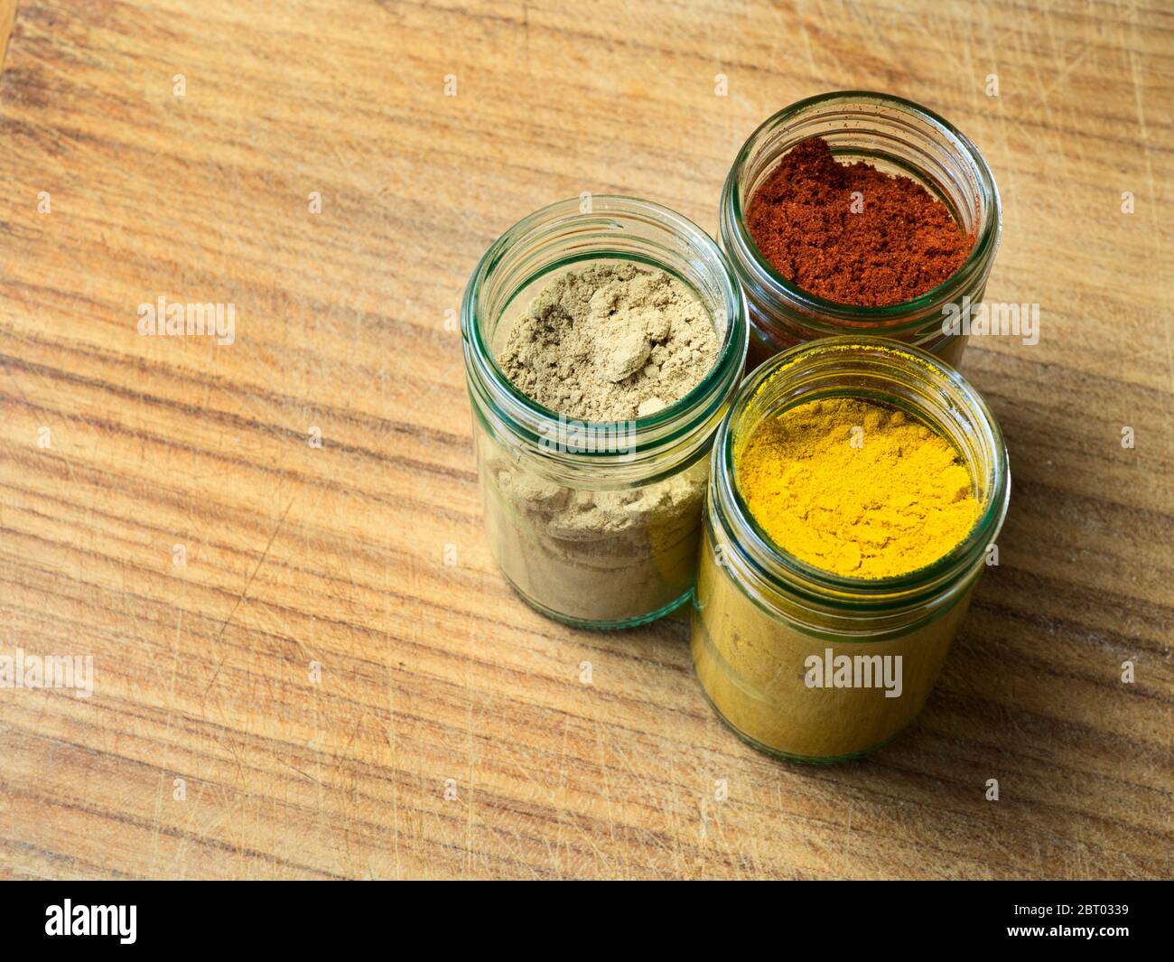 Gläser mit gemahlenem Ingwer, scharfem Chilipulver und Kurkuma auf einem Holzbrett mit Kopierfläche Stockfoto