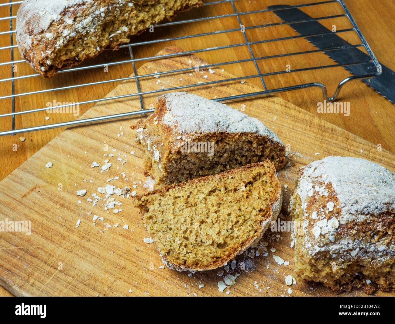 Frisch gebackenes Sodabrot, das auf einem hölzernen Brotscheiben mit einem halben Laib auf einem Drahtscheiben geschnitten wurde Stockfoto