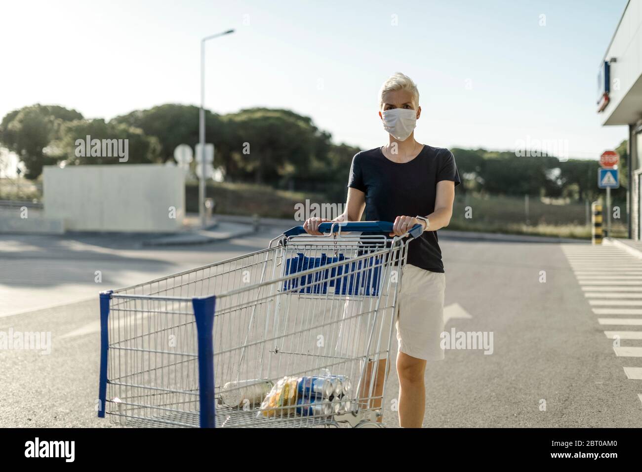 Frau mit schützender Gesichtsmaske mit Warenkorb vor dem Supermarkt Stockfoto