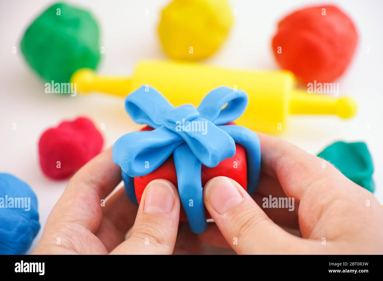 Kind halten spielen Ton Geschenk mit blauem Band verpackt. Geschenkbox und Band sind aus Spielton (Plastilin). Stockfoto