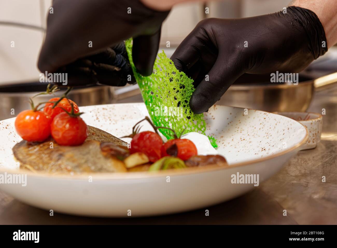 Der Koch schmückt ein Fischgericht mit grünen Käsechips Stockfoto