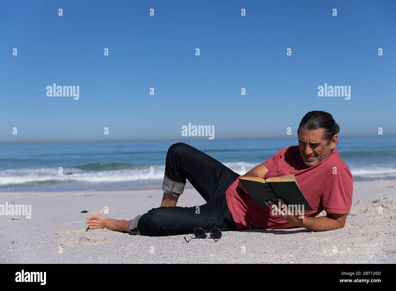 Älterer kaukasischer Mann, der ein Buch am Strand liest. Stockfoto