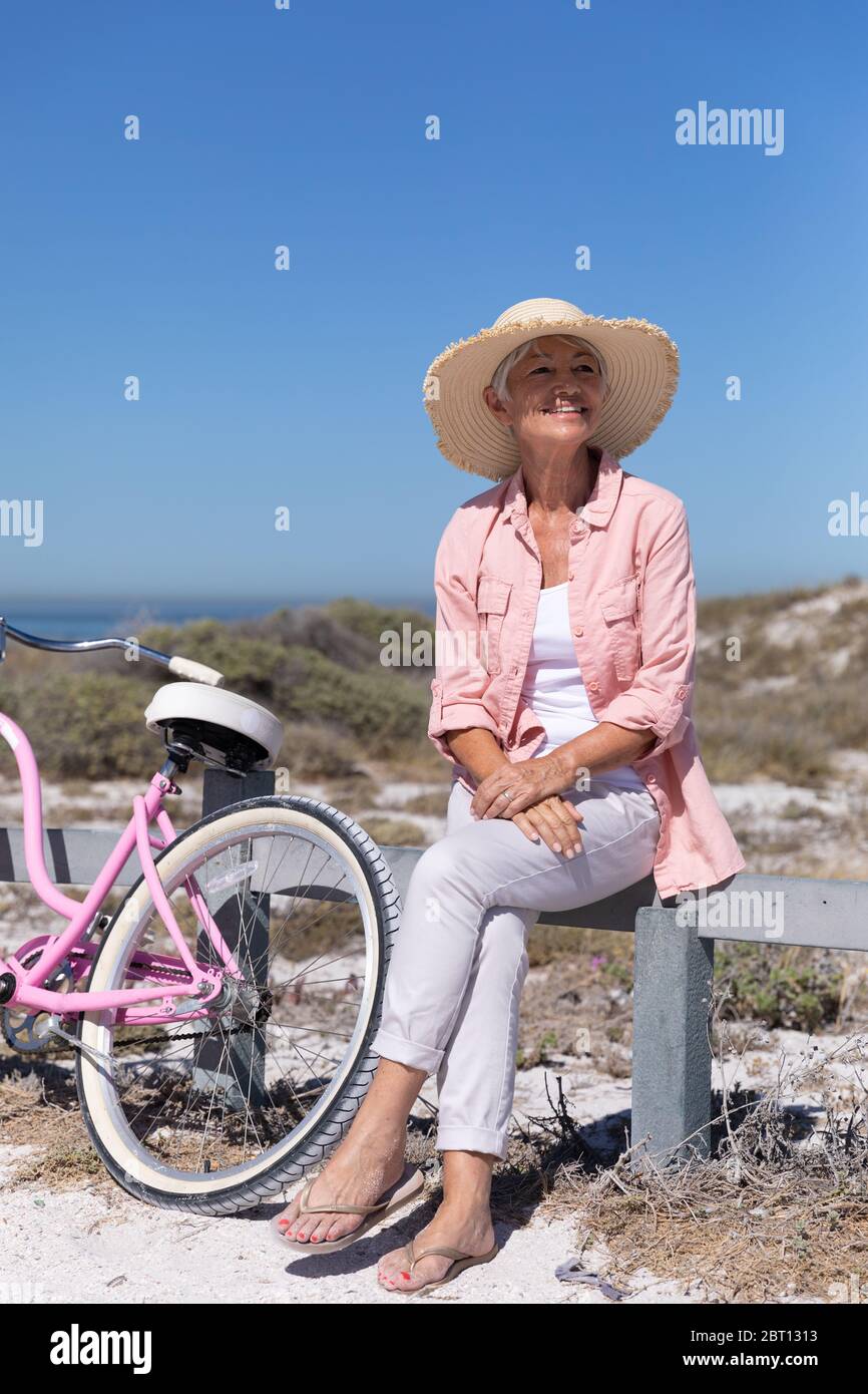 Ältere kaukasische Frau sitzt auf einer Barriere am Strand. Stockfoto