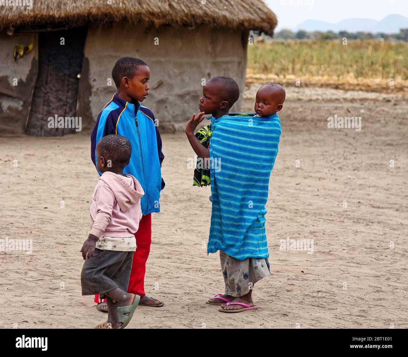 Vier Maasai-Kinder, Dorf; Ureinwohner; kleines kreisförmiges Schlammhaus, Schmutz, Feld, entfernter Berg, Tansania; Afrika Stockfoto