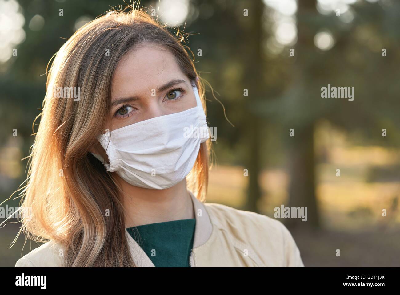 Junge Frau trägt weiße Baumwolle Virus Mund Nasenmaske, verschwommenen Park und Bäume Hintergrund, Nahaufnahme Gesicht Porträt, Coronavirus covid 19 Ausbruch preven Stockfoto