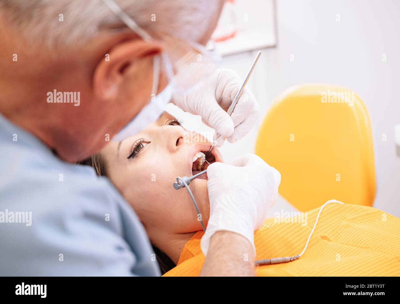 Erwachsener Mann mit professionellen zahnärztlichen Werkzeugen, um Zähne der jungen Dame während der Arbeit in der modernen Klinik zu heilen Stockfoto