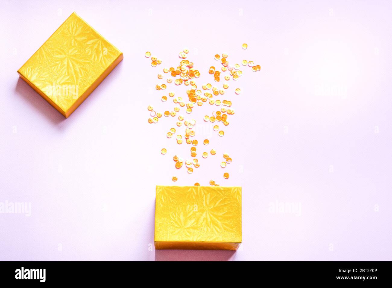 Gelbe offene Geschenkbox mit verschiedenen Party Konfetti auf rosa Hintergrund. Farbenfrohes Festkonzept. Flaches Lay. Stockfoto