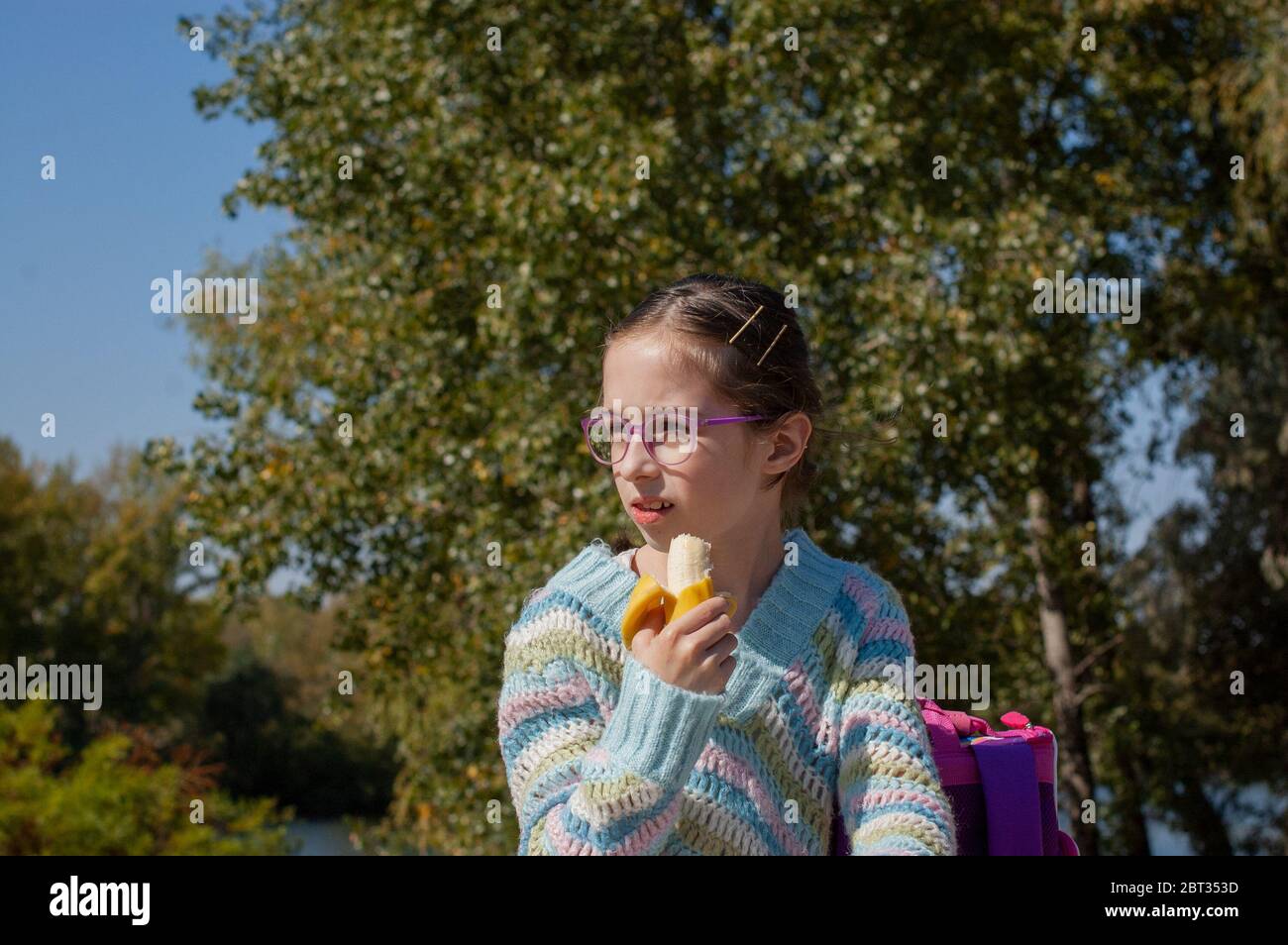Schulmädchen, das eine Banane auf der Straße isst. Alpha Generation Kinder werden die treibende Kraft hinter dem Fortschritt in unserem Jahrhundert. Sie sind ausgewogener, Stockfoto