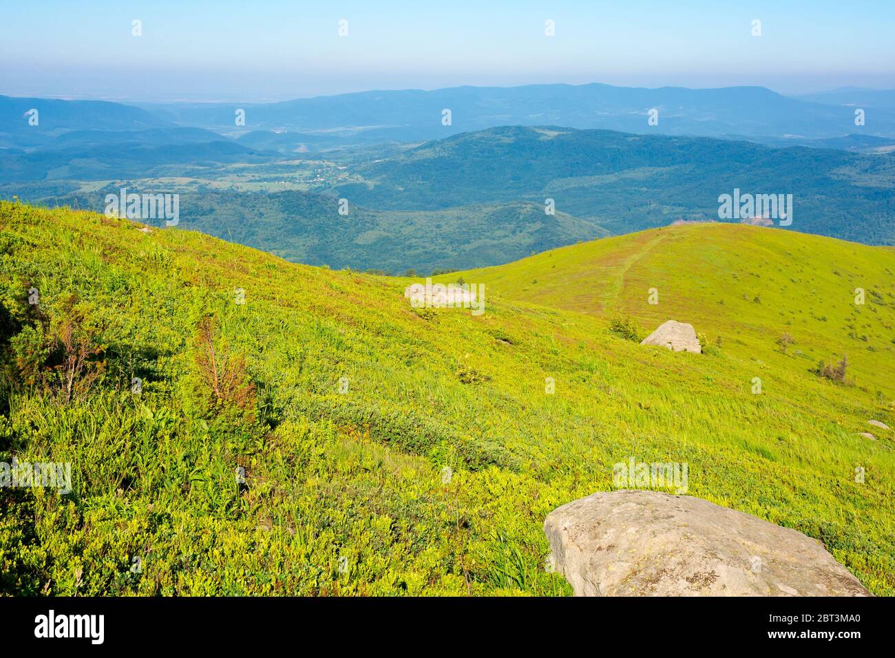 Bergsommerlandschaft. Wiese mit Riesen scharfen Stein unter dem Gras am Rande eines Hügels Stockfoto