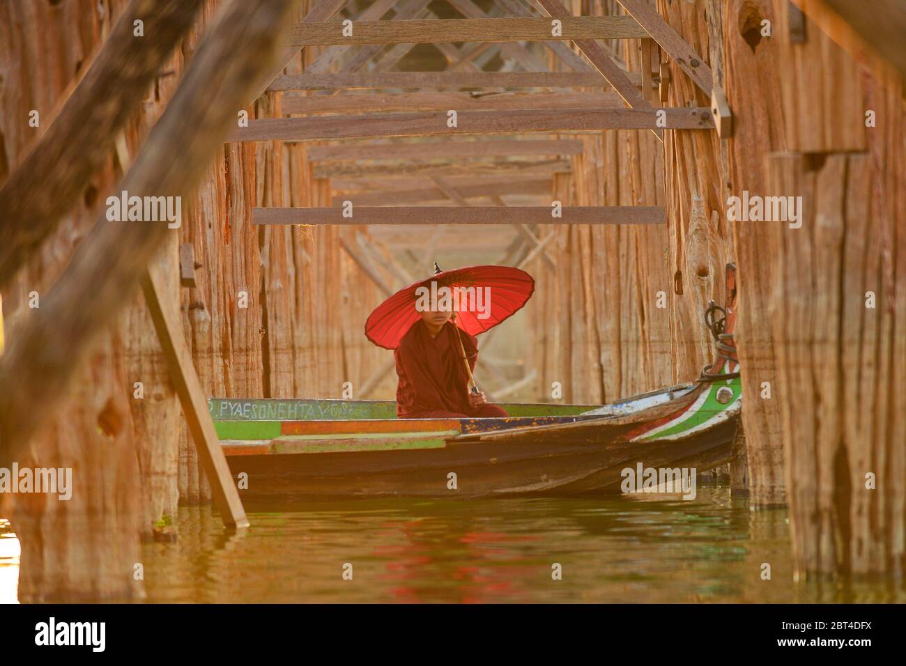 Novize Mönch in einem Boot unter U Bein Brücke bei Sonnenaufgang, Mandalay, Myanmar Stockfoto