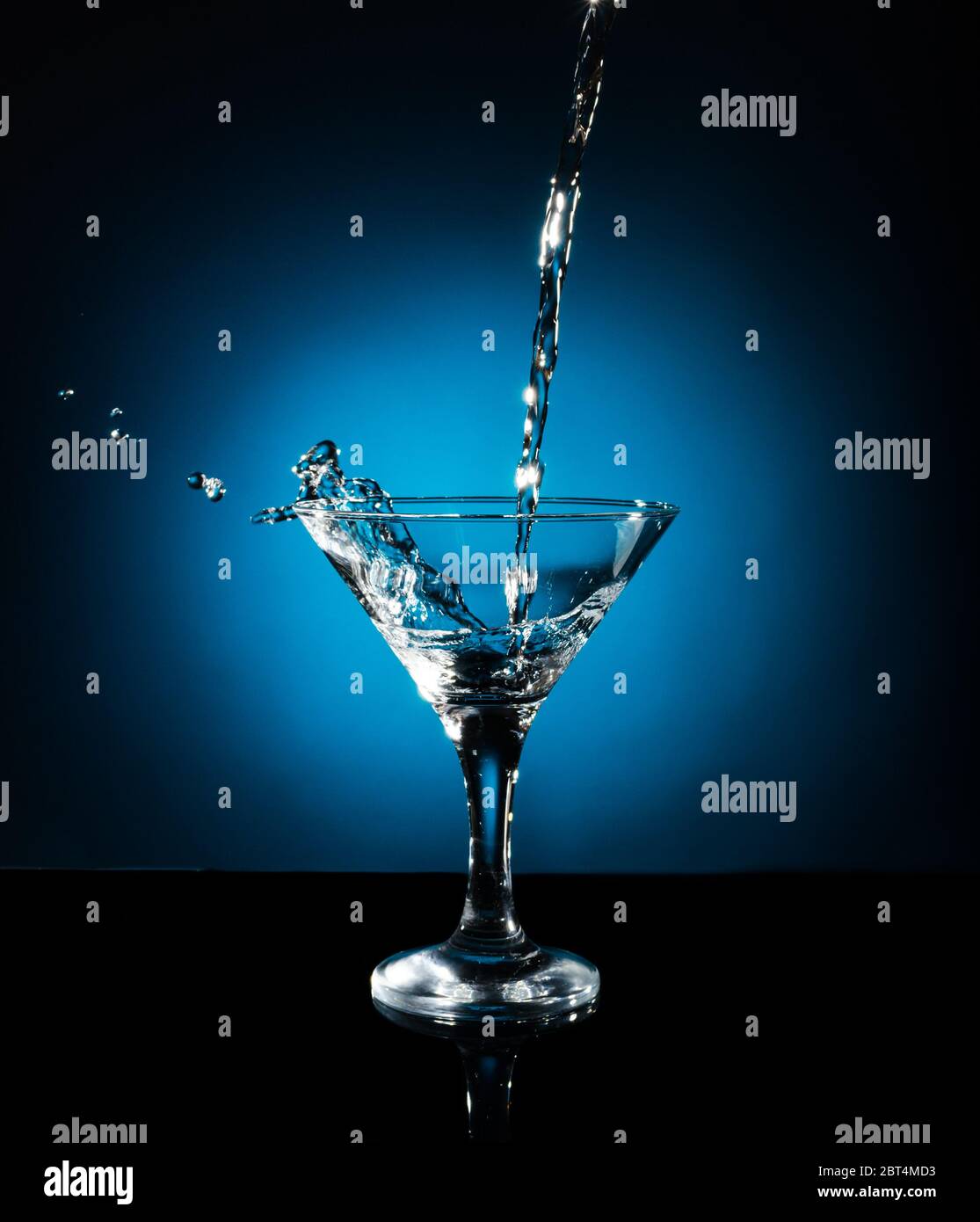 Spritzen Sie aus dem Gießen von martini ins Glas. Objekt auf blauem Hintergrund Stockfoto