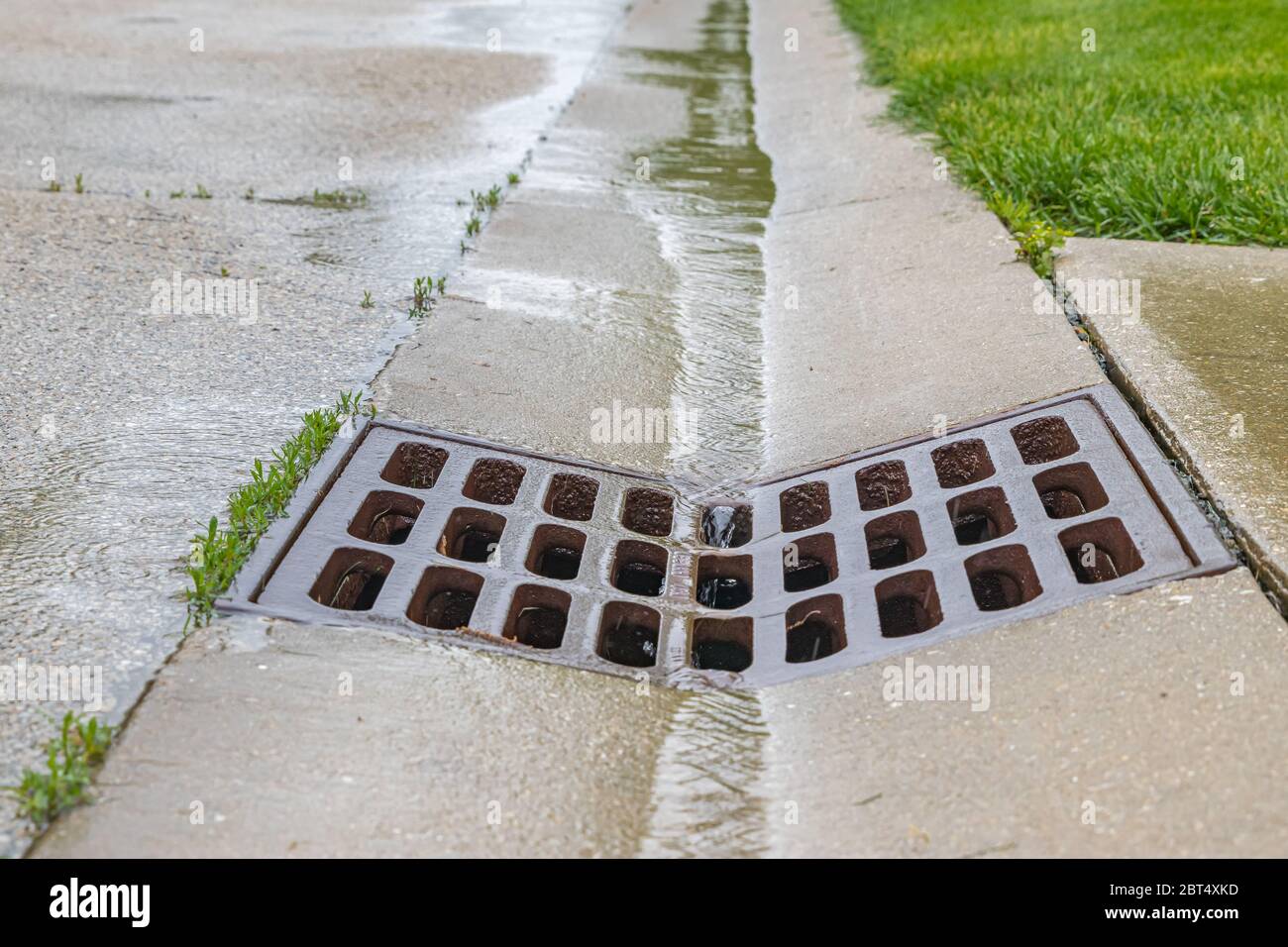 Nahaufnahme von Regenwasser, das in die Rinne der Straße fließt und in das Regenwasserkanalrost fließt. Stockfoto