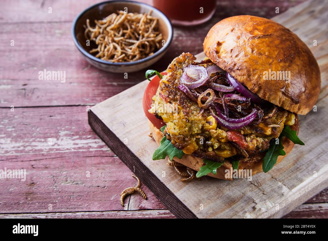 Knusprig gebratener mealworm Insekt Burger auf einem frischen Brötchen mit Salat Beilagen und eine Beilage der Würmer auf einem rustikalen Holztisch mit Kopie Raum serviert. Stockfoto