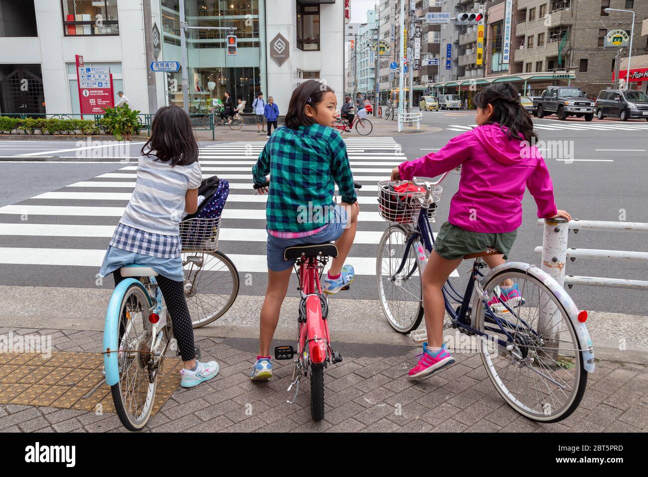 Tokio, Japan - 20. April 2020: Drei Kinder mit Freundinnen aus Japan fahren Fahrrad und halten vor der Überquerung an der Ampel am Fußgängerüberweg Stockfoto