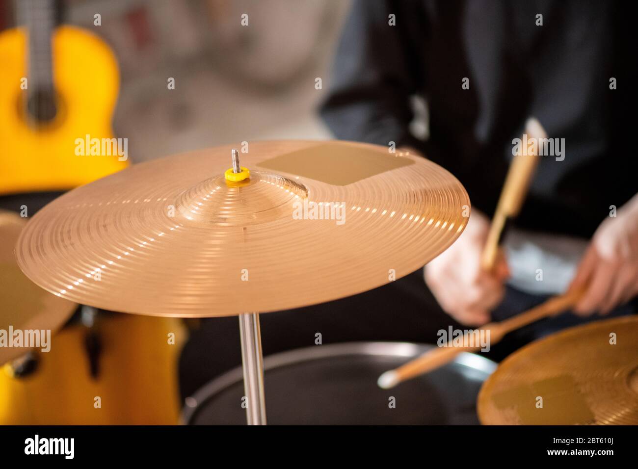 Runde goldfarbene Becken als Teil des Drumsets auf Hintergrund des zeitgenössischen Musikers in schwarzem Sweatshirt während der Probe Stockfoto