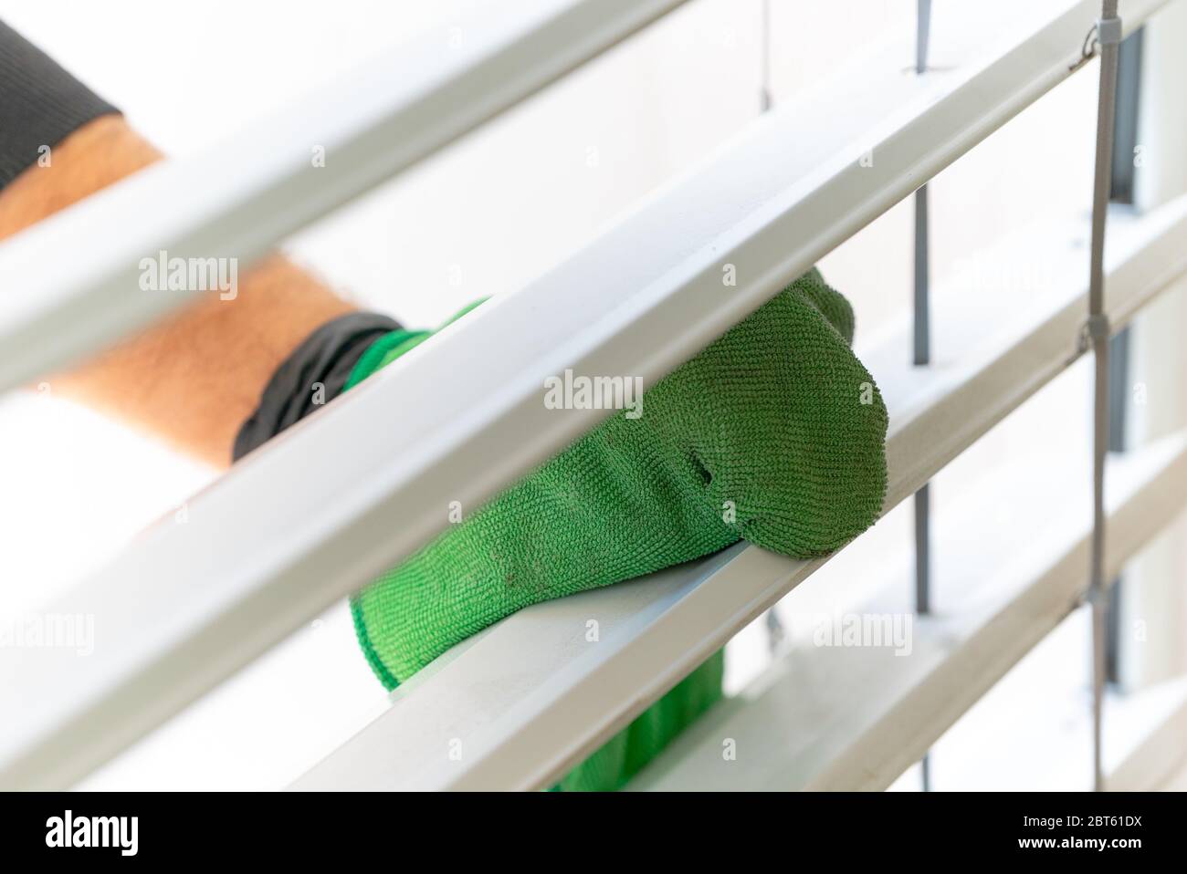 Eine Nahaufnahme eines professionellen Reinigers, der Fensterläden in einer Wohnung mit einem grünen Mikrofasertuch reinigt Stockfoto